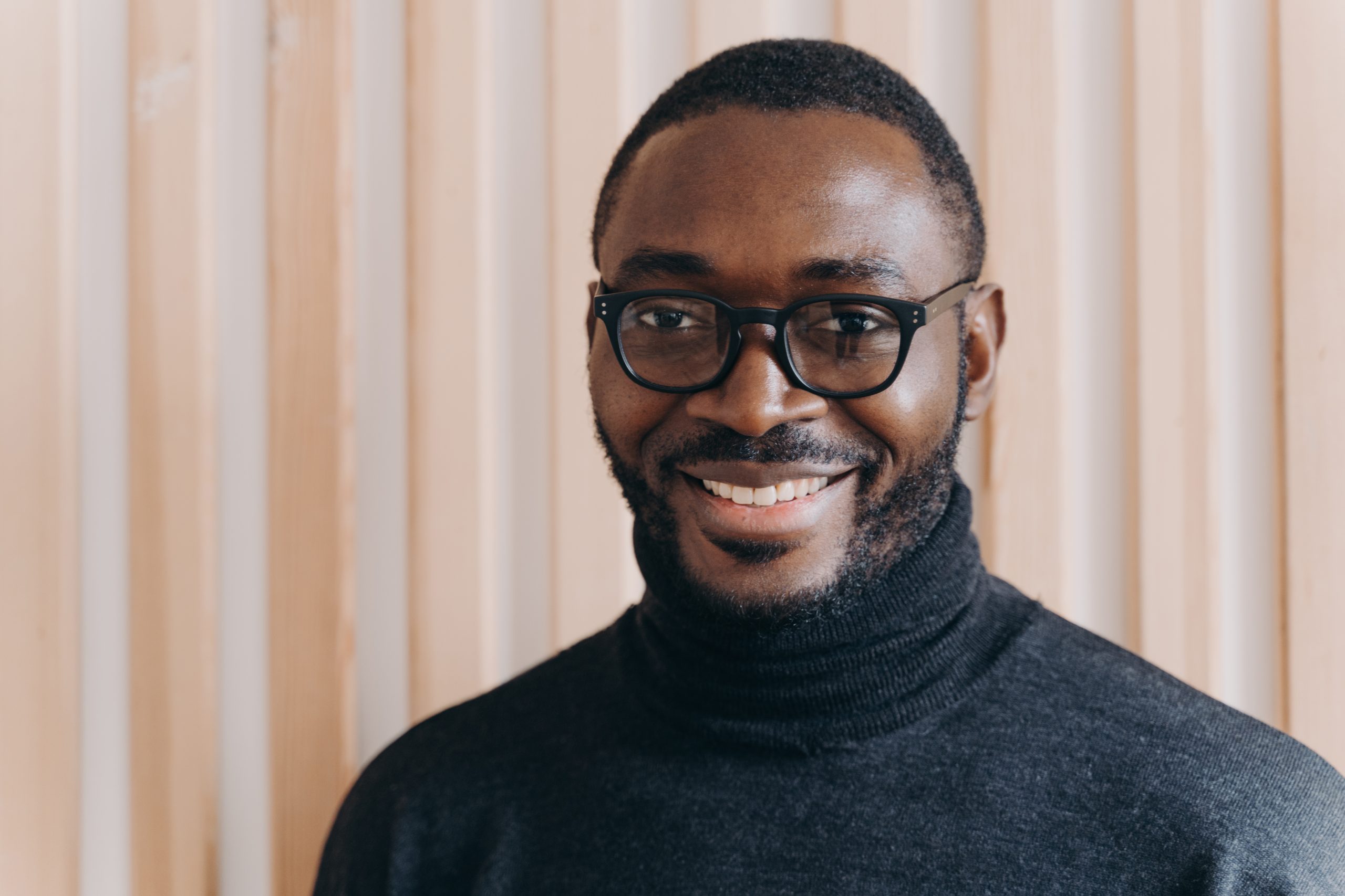 Close up portrait of elegant confident African american businessman in glasses posing while standing in modern office, looking at camera smiling broadly and sincerely, happy with company progress